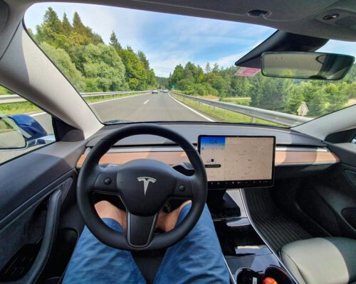 Driving down an empty highway in a high-tech autonomous Tesla vehicle. Young man drives along a scenic rural motorway hands-free in a modern self-steering car.