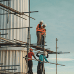 A construction crew in hard hats and safety vests standing on scaffolding.